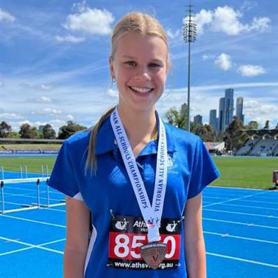 Anika smiling with her bronze medal at the track